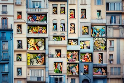 The artist has created what looks to be a concrete building façade, with each window filled with cutout images ranging from a human skull to a superhero to a woman in an evening gown.